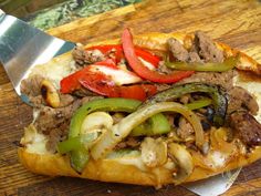 a pizza with meat, peppers and onions on it sitting on a cutting board next to a knife