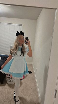 a woman in a costume taking a selfie with her cell phone while standing in a bedroom