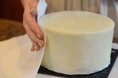 a woman is decorating a cake with white frosting on the top and bottom