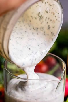 a person pouring dressing into a glass bowl with vegetables in the backgroung