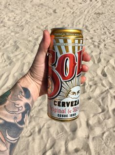 a person holding up a can of beer on the beach