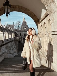 a woman is walking down the stairs with her hand in her hair and wearing a fur coat