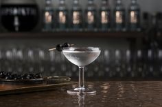 a martini glass with an olive garnish on the rim next to a tray of black olives