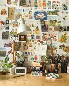 a cluttered desk with lots of pictures on the wall and a lamp above it