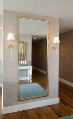 a large mirror sitting on top of a wooden floor next to a white table and two lamps