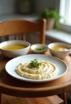 hummus and carrots are served on a white plate with two bowls of soup in the background