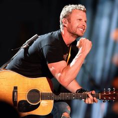 a man holding a guitar and singing into a microphone while wearing a black t - shirt