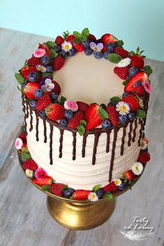 a decorated cake sitting on top of a metal stand with flowers and chocolate drizzle