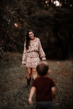 a woman in a floral dress is walking with a small child through the grass and trees