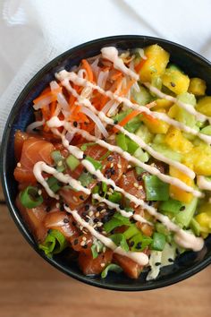 a black bowl filled with salad and dressing on top of a wooden table next to a white towel