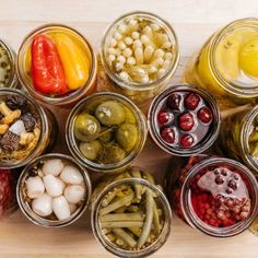 many jars filled with different types of food on a wooden counter top, including beans, peppers, and other vegetables