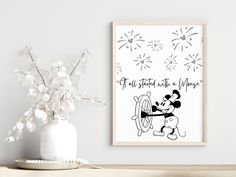 a mickey mouse poster on the wall next to a vase with white flowers in it