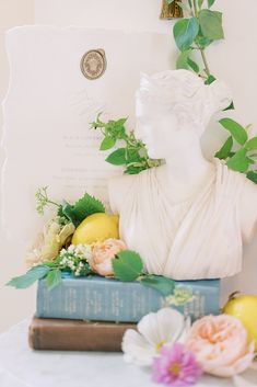 a white busturine sitting on top of a stack of books next to flowers