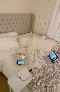 an unmade bed with two laptops on top of it and a phone in the middle