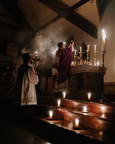 the priest is lighting candles at the alter with his arm in the air as people look on