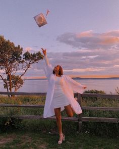 a woman in a white dress is throwing a graduation cap into the air over her head