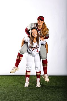 two women in baseball uniforms are posing for a photo on the field with their arms around each other