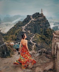 a woman in a colorful dress sitting on top of a mountain looking at the sky