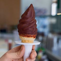 a hand holding an ice cream cone with chocolate frosting on it's tip