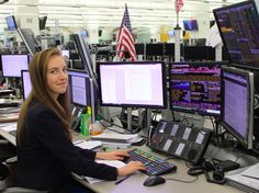 a woman sitting at a desk in front of multiple computer monitors