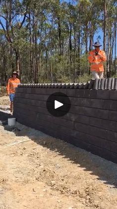 two men in orange shirts are working on a wall with cement and concrete mortars