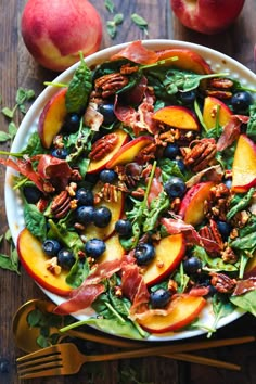 a salad with peaches, blueberries and pecans on a plate next to two forks