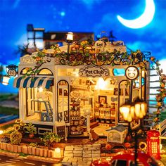 a miniature model of a store with lights and decorations on the front, next to a red car