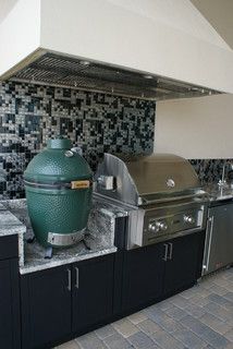 an outdoor kitchen with stainless steel appliances and tile backsplash, including a large green egg