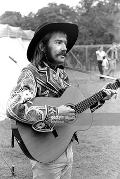 a man wearing a cowboy hat and holding an acoustic guitar in his right hand while standing on the grass