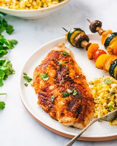 a white plate topped with meat and veggies next to a bowl of rice