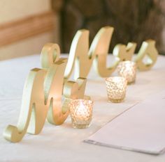 candles are lined up on a table with gold ribbons and glass votives in front of them