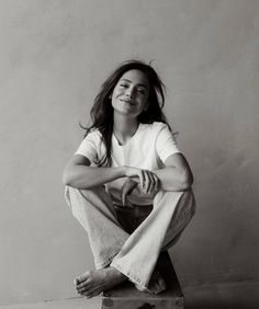 a young woman sitting on top of a wooden box with her legs crossed and smiling