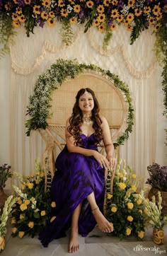 a woman in a purple dress sitting on a wicker chair surrounded by flowers and greenery