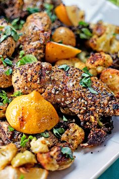 a white plate topped with meat, potatoes and oranges on top of a table