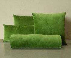 two green pillows sitting next to each other on top of a gray table with a white wall in the background