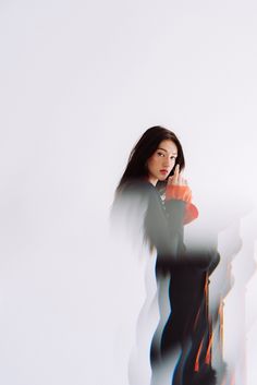 a woman standing in front of a white wall talking on a cell phone