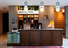 a woman behind the counter in a store with lights on and rugs covering the floor