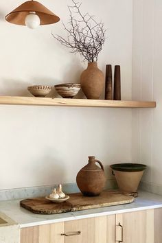 two wooden shelves with vases and bowls on them in a white kitchen, next to a light fixture