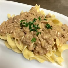 a white plate topped with pasta covered in meat sauce and garnished with parsley