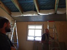 two men standing in a room with ladders on the ceiling and one man holding a paint roller