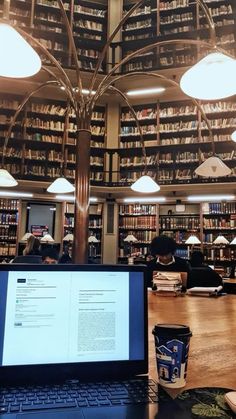 a laptop computer sitting on top of a wooden table in front of a library filled with books