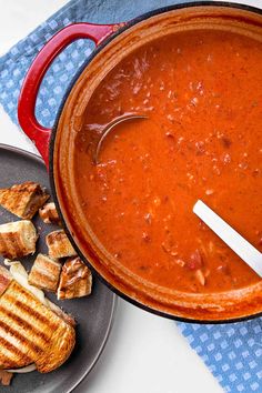 a pot of tomato soup with grilled bread on the side