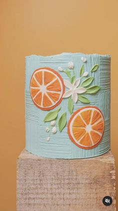 a cake decorated with oranges and flowers on top of a wooden block in front of a wall