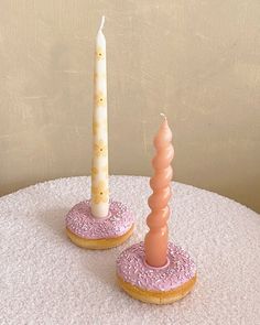 two donuts with frosting and sprinkles are on a table next to a candle