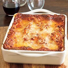 a casserole dish on a wooden table with wine glasses