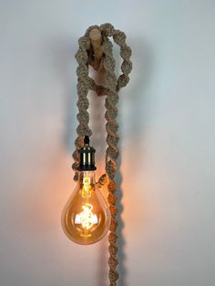 a light bulb hanging from the side of a wall with rope wrapped around it's sides