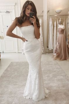 a woman in a white wedding dress taking a selfie while looking at her cell phone