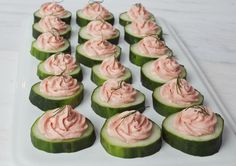 cucumbers with pink whipped cream on them sitting on a white platter, ready to be eaten