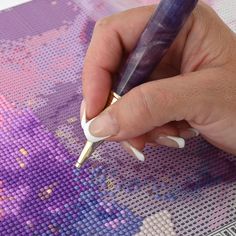 a woman's hand holding a pen over a cross stitch pattern