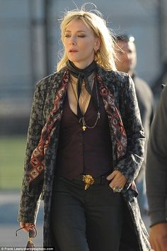 the blonde woman is walking down the street with her hand on her hip and wearing a scarf